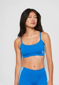 Top corto atlético azul con tirantes finos, hecho de una tela suave. Presenta franjas laterales blancas y un pequeño logo en la parte delantera.