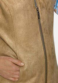 Beige Faux-Suede-Weste mit einem eleganten Reißverschluss, Taschen an der Seite und einer glatten Textur. Verfügt über eine taillierte Passform mit Nahtdetails entlang der Nähte.