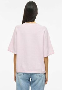 Roza pulover s kratkimi rokavi iz mehke tkanine, z sproščenim krojem in rebrastim robom, kombiniran s svetlo modrimi kavbojkami z visokim pasom.