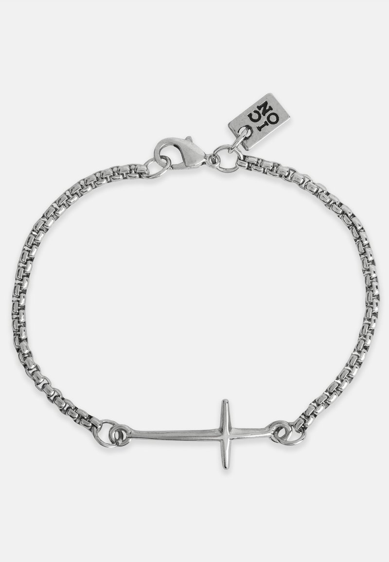 Sidabrinė grandinėle apyrankė, turinti horizontalų kryžiaus pakabuką. Grandinės akys yra apvalios, o užsegimas yra omaro tipo su prekės ženklo etikete.