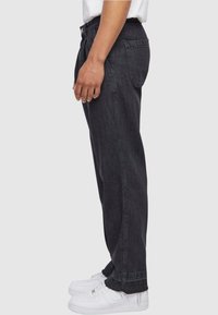 Jeans de mezclilla negros, de corte relajado y piernas rectas, con bolsillos laterales y detalles de costura, combinados con zapatillas blancas.
