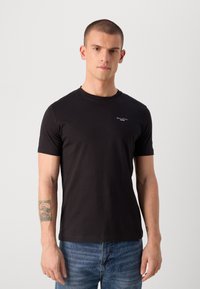 Tricou negru cu mânecă scurtă, din bumbac, cu guler rotund și un mic logo alb pe pieptul stâng. Poartă-l cu blugi albaștri.