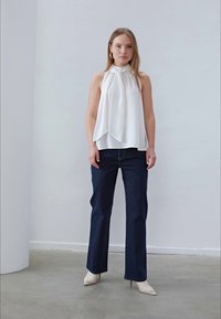 Vit linne utan ärmar med draperad design, kombinerat med mörkblå raka jeans och vita spetsiga klackar. Enkla, rena linjer och texturer.