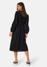 Zwarte midi-jurk met pofmouwen, een gesmockte taille en een bloempatroon. Gemaakt van lichtgewicht stof met een vloeiende silhouette.