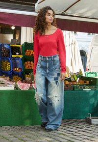 Rode lange mouw top met een ronde hals, gecombineerd met oversized versleten denim jeans met patchaccenten en rafelige randen. Zwarte schoenen.