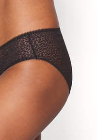 Sorte spiler med en glatt tekstur, med en scallopkant og intrikate blomstermønstre, formet for å sitte komfortabelt.