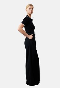 Zwarte, aansluitende top met witte kraagdetails, gecombineerd met zwarte broek met wijde pijpen. Gladde textuur, eenvoudig ontwerp en geen zichtbare patronen.