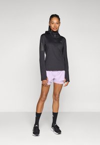 Haut noir à manches longues avec un col montant et une fermeture éclair devant, associé à un short violet clair. Des chaussures de sport noires et des chaussettes complètent le look.