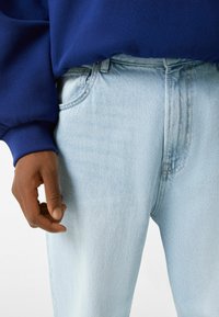 Ljust blå denimjeans med rak benform. Funktioner inkluderar en övre knapp, framfickor och synliga sömmar.