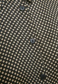 Svart tygskjorta med ett vitt prickmönster, försedd med en svart knapp och krage, slät textur och skräddarsydd passform.