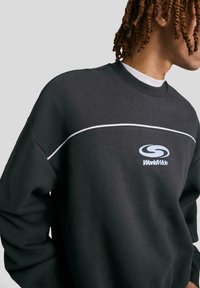 Felpa nera con linea d'accento bianca e logo "WorldWide". Presenta una vestibilità rilassata e un colletto a costine, realizzata in morbido cotone.