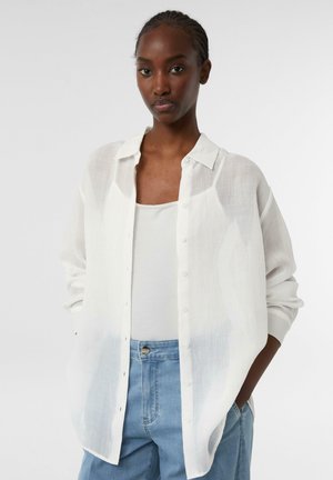 White lightweight, semi-translucent shirt with a button-up front and long sleeves, paired with a gray tank top and blue jeans.