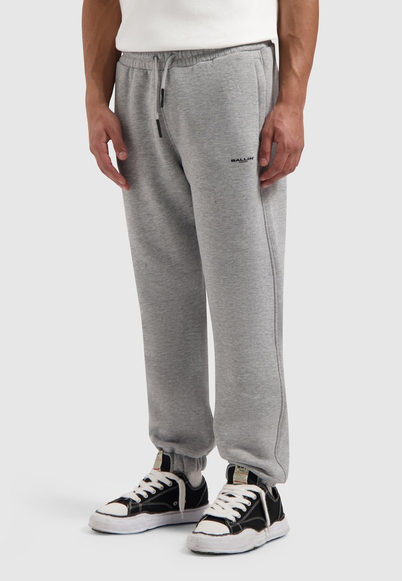 Grijze sweatpants van zachte stof, met een tailleband met trekkoord en een logo. Gecombineerd met zwart-witte sneakers met een gestructureerd oppervlak.