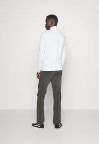 Hvit langermet høyhalset skjorte kombinert med grå bukser og svarte joggesko med hvite aksenter, med en glatt tekstur og minimalistisk design.