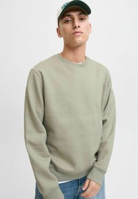Lichtgroene sweatshirt met een ronde hals, geribbelde manchetten en onderrand. Soepele textuur, gecombineerd met blauwe denim jeans en een wit onderhemd.