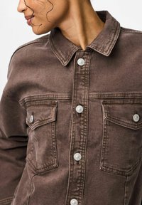 Brun denimjakke med klassisk krave, frontknaplukning og to brystlommer med trykknapper. Glat tekstur og afslappet design.