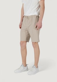 Pantaloni sportivi beige con elastico in vita e cordoncino, dotati di tasche laterali e una texture liscia, abbinati a sneakers bianche.