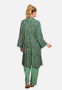 Groene bloemen kimono met lange mouwen en een strik taille, gecombineerd met groene en witte gestreepte broek en bruine instap schoenen.