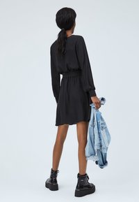 Svart långärmad klänning med samlad midja, lager av textur och skaterkjol, tillsammans med en ljusblå denimjacka. Svarta plattformsstövlar.