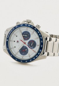 Sølv chronograf armbåndsur med hvid urskive, blå tachymeter bezel, tre blå underdials og metal link armbånd.