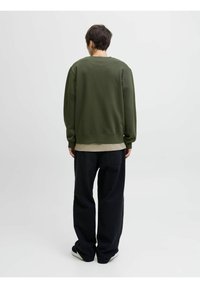 Groene sweatshirt met een ronde hals, lange mouwen en geribbelde manchetten, gecombineerd met losse donkere broek en zwarte schoenen.