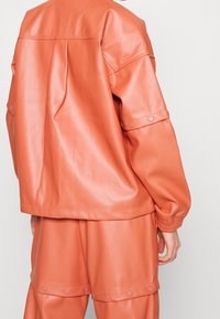 Giacca oversize in pelle corallo caratterizzata da una texture liscia, polsini a coste e dettagli con bottoni a pressione sulle maniche.