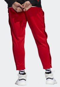 Rode sportieve broek met zijsnapsluitingen, gemaakt van gladde stof. Gecombineerd met witte sneakers en zwart-witte gestreepte sokken.