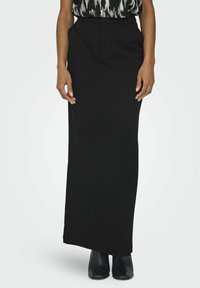 Jupe maxi noire ajustée avec une texture lisse et une fente latérale subtile, associée à un haut à motifs et à des bottes noires longueur cheville.