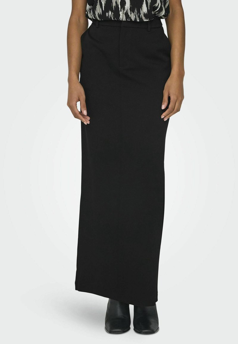 Jupe maxi noire ajustée avec une texture lisse et une fente latérale subtile, associée à un haut à motifs et à des bottes noires longueur cheville.