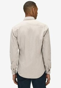 Ljusbeige långärmad skjorta med ryggsöm, knappade ärmslut och en böjd nederkant. Tillverkad av ett mjukt tyg med en subtil textur.