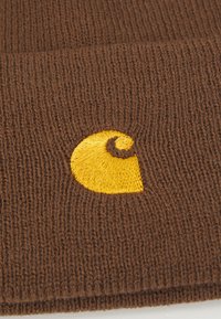 Bruine gebreide beanie met een gestructureerde stof. Bevat een gele geborduurde logo in de vorm van een gestileerde "C" nabij de onderkant.