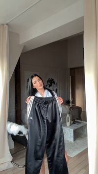 Juodos satino treniruotės kelnės su baltomis šoninėmis juostomis ir elastinga juosmena. Kairėje šlaunyje yra mažas logotipas. Lygus paviršius.