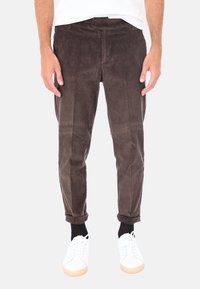 Pantaloni in corduroy marrone con righe verticali, slim fit, risvolti e tasche, abbinati a sneakers bianche e calzini neri.