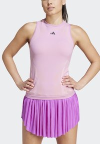 Roze mouwloos topje met textuurdesign en logo, gecombineerd met een paarse geplooide rok. Beide elementen zijn gemaakt van atletisch stof.
