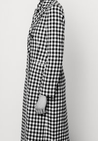 Zwart-witte geruite jas met een getailleerd ontwerp, lange mouwen, reverskraag en zijzakken. De stof heeft een gedurfd ruitpatroon.