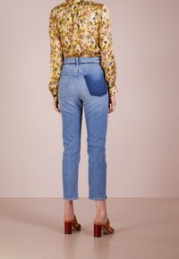 Jeans in denim azzurro chiaro con vita alta, vestibilità dritta e una tasca blu a contrasto. Abbinati a una blusa floreale a maniche lunghe e sandali.