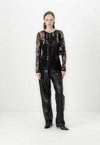 Sheer black lace long-sleeve top layered over a black camisole, paired with high-waisted black leather pants featuring metal accents.