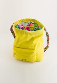Geantă din țesătură galbenă, cu un interior decorat și curea multicoloră. Geanta are o buzunar frontal și un design lejer.