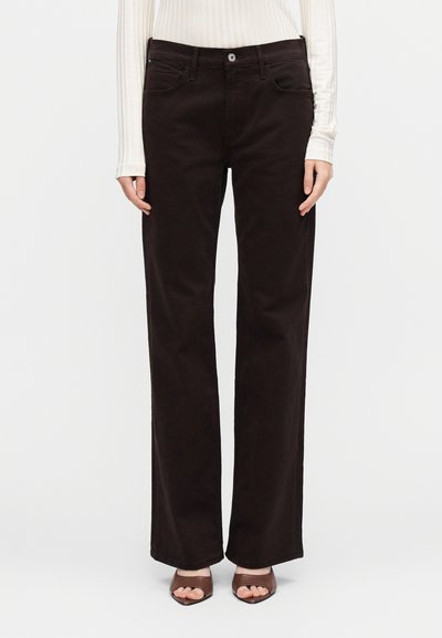 Rjave široke hlače iz mehkega materiala, z žepi spredaj in zapiranjem na gumbe. Nošene s oprijetim belim dolgim rokavom.