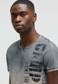 Gray short-sleeve T-shirt with a V-neck, featuring dark text and logo accents on the left side and a faded texture.