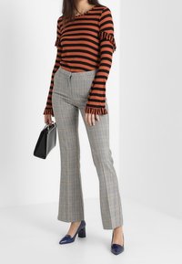 Randig orange och svart tröja med volangärmar, kombinerad med grå rutiga utsvängda byxor. Accessoarer inkluderar en svart handväska och blå klackskor.