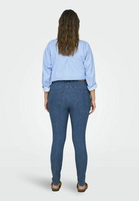 Modré džíny skinny s polovičným pásom, so zadnými vreckami a viditeľným šitím. Nosí sa s svetlomodrou pruhovanou košeľou s golierom.