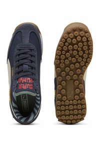Zapatillas de ante azul marino con acentos en blanco y amarillo, que presentan una suela de goma texturizada y un patrón interior a rayas. Texto: "SUPER PUMA."