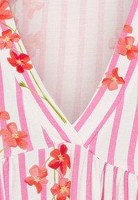 Klänning med V-ringning i mjukt tyg med rosa och vita vertikala ränder, accentuerad med röda och orange blommönster längs kragen.