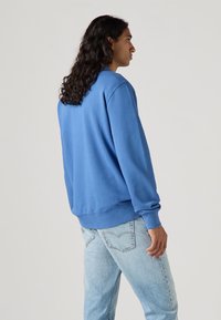 Blue sweatshirt made of soft fabric, featuring a crew neck, long sleeves, and ribbed cuffs. Paired with light blue denim jeans.