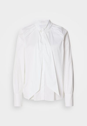 Blusa blanca de mangas largas con un escote de lazo, que presenta una textura suave y un diseño frontal plisado. Las mangas con puños completan el look.