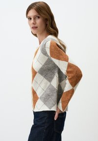 Cardigan en tricot avec un motif argyle orange, gris et blanc. Design en V avec des manches longues et une coupe décontractée.