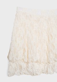 Spetskjol i off-white med lagerdesign, vågig nederkant och elastisk midja. Mönstrad spetsstruktur genom hela kjolen.