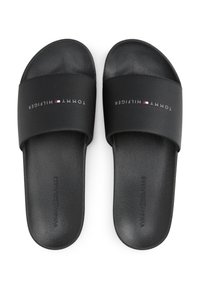 Svarte slidesandaler med en teksturert stropp som har "TOMMY HILFIGER" logo, akkompagnert av et lite rødt, hvitt og blått flagg. Teksturert såle.