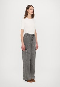 Bredde bukser i cargo-stil i grå denim, med lap pockets, høy midje og en avslappet passform, kombinert med en tettsittende hvit t-skjorte med korte ermer.